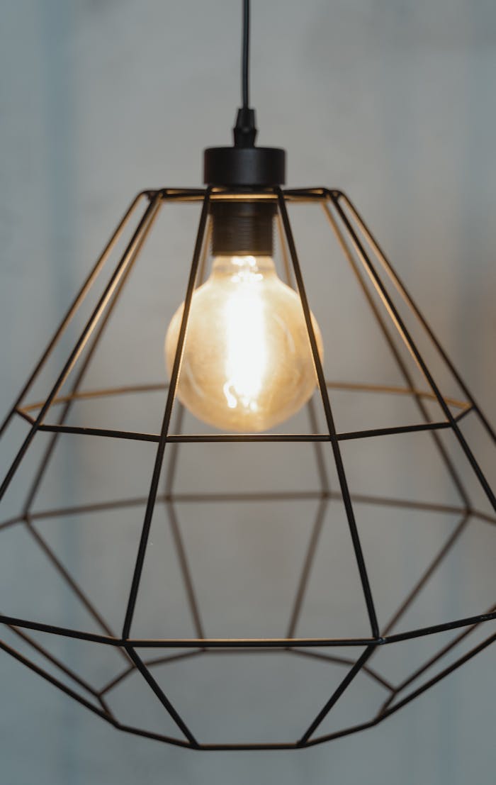 Close-up of a modern industrial cage pendant light with an exposed bulb, showcasing minimalist design.