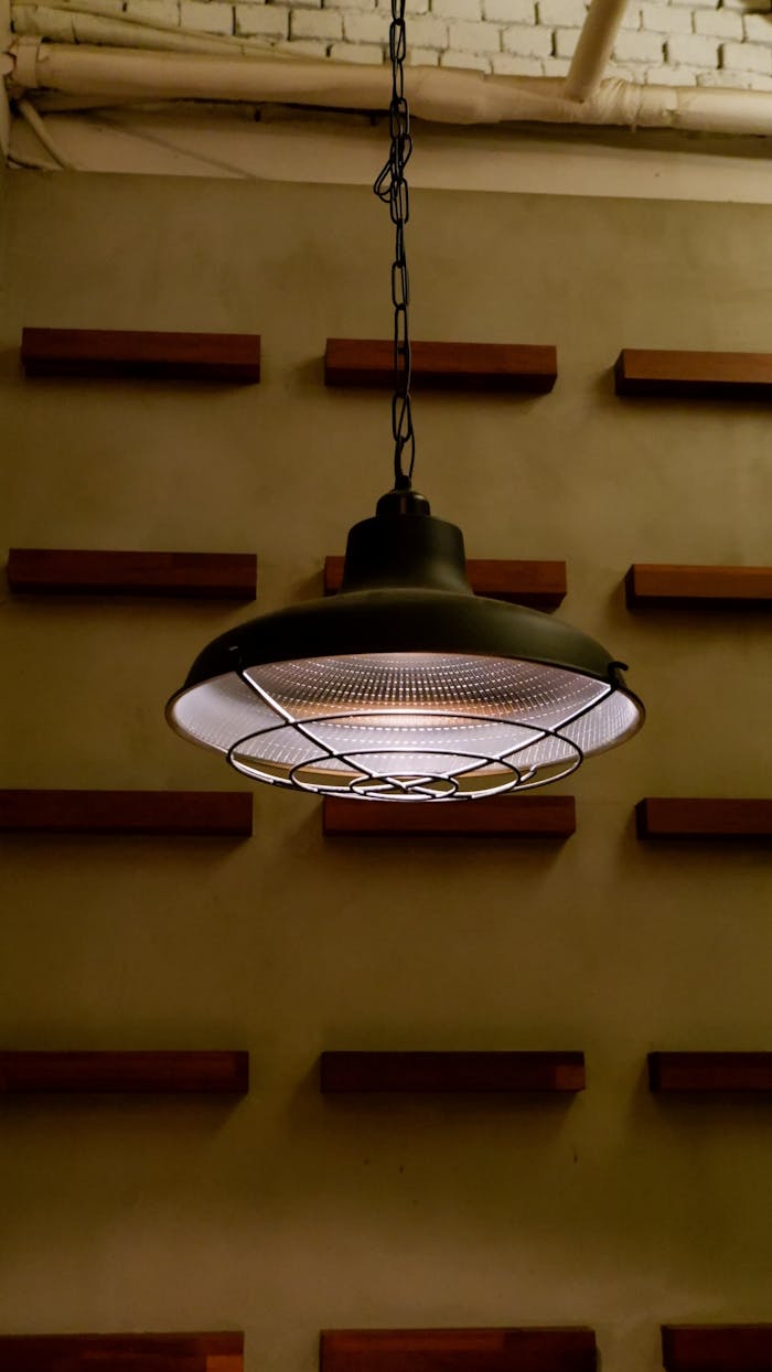 A retro-style pendant lamp hanging with a warm glow against a textured wall with wooden elements.